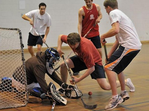 Several floor hockey players fight for control of the ball near the net as the goalie defends