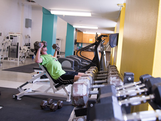 A man lifts weights in the Henderson Fitness Centre surrounded by rows of exercise equipment