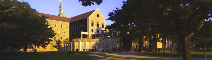 An exterior view of the front of the Tyndale building, trees, and front lawn, lit by the sun