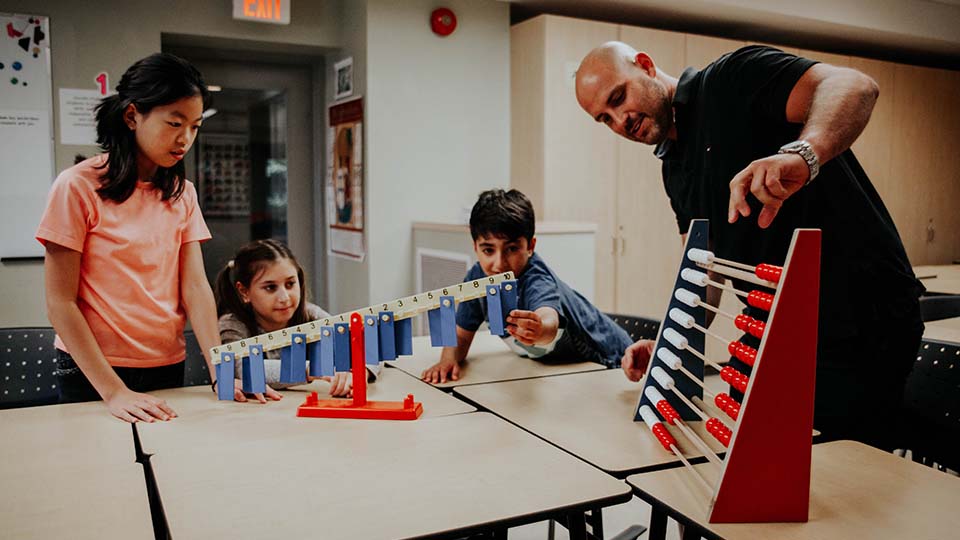 A male teacher plays with an abacus teaching three young children