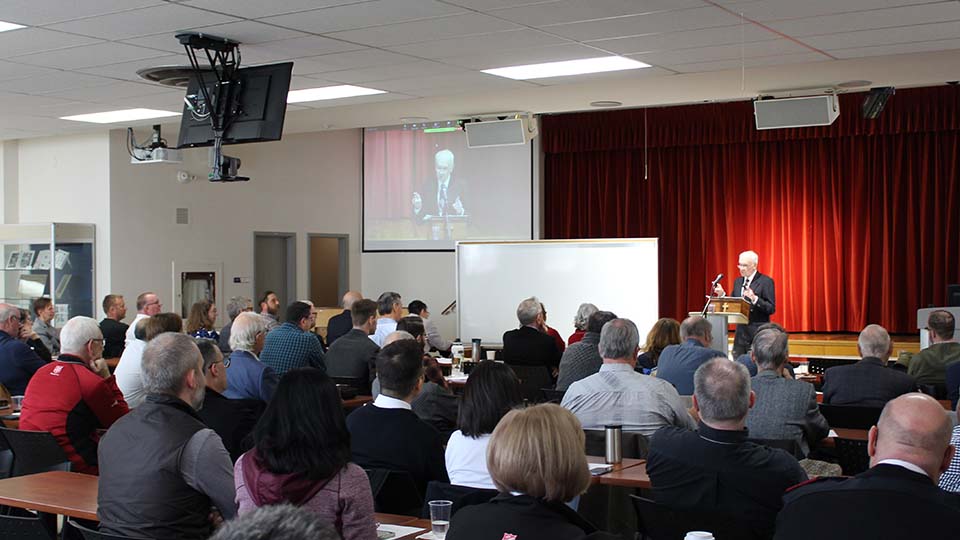 A group of men and women listening to a man on a podium