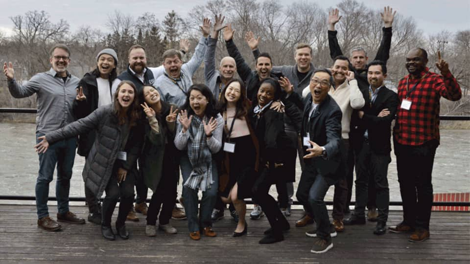 Group of men and women smiling with their hands up on a deck