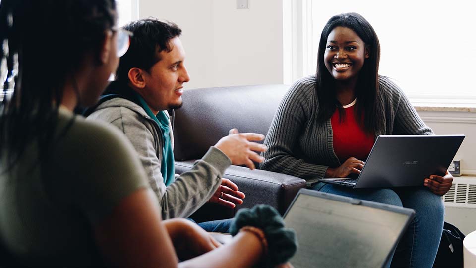 A group of students sitting down having a discussion with their laptops