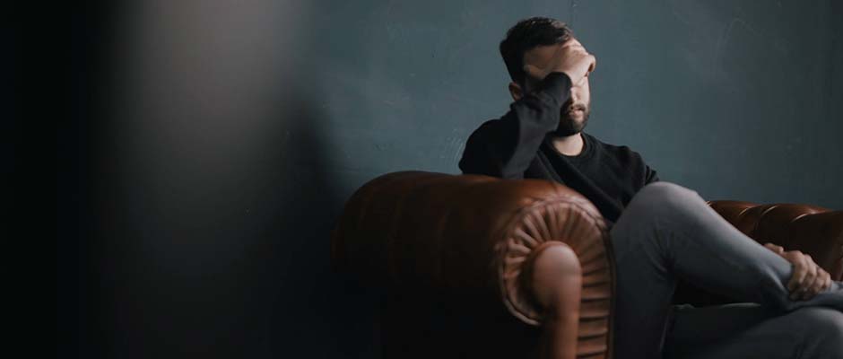 a man holds his head while sitting on sofa