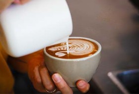 A cup of milk poured into a cup of coffee held by a hand