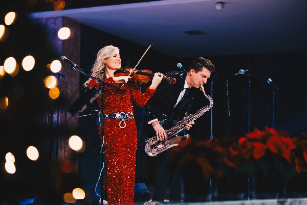 Woman dressed in red playing a violin with a man dressed in a shiny tuxedo playing a saxaphone