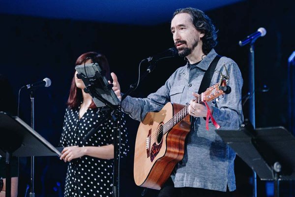 Dr. Ken Michell playing guitar leading congregation in song and scripture reading