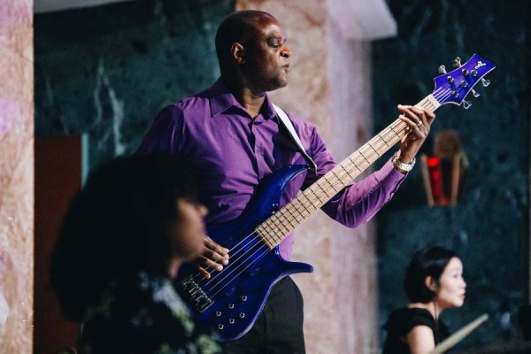 Wayne Thompson, bassist strums bass chord alongside Abigail Ali and Dr. Joy Lee