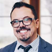 Man with bold black glasses smiling in a suit and tie